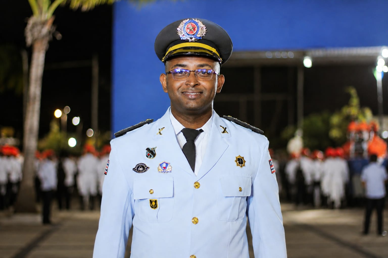 Registro da época na PMMA com uniforme de gala branco e quepe, em ambiente externo à noite